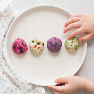 four oatmeal with vegetables rolled into balls with a baby's hand touching one.